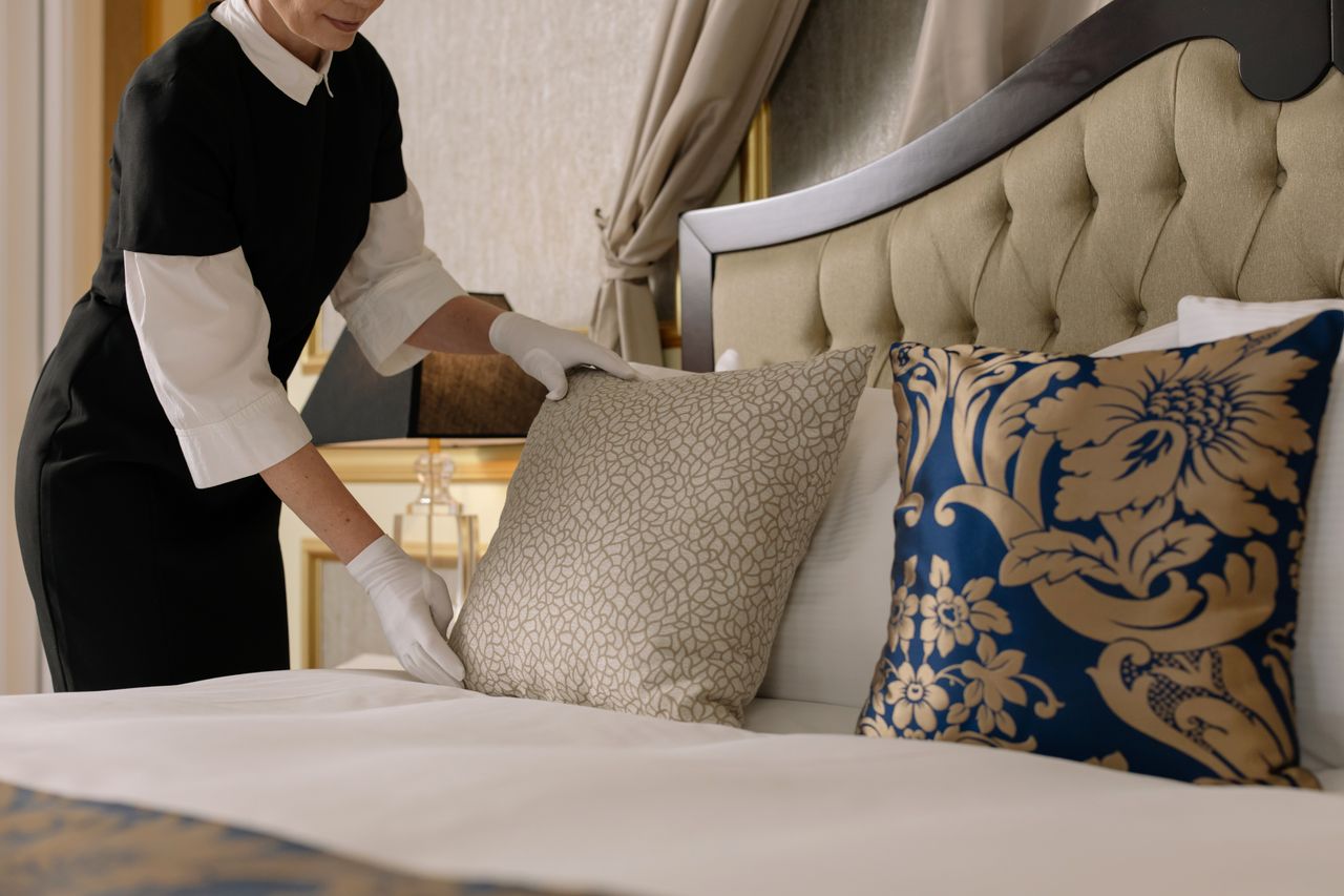 our-story A chambermaid arranges pillows in a luxurious hotel room, showcasing comfort and elegance.