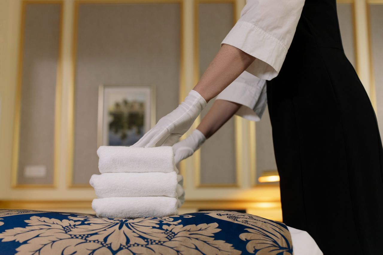 gallery-01 A hotel housekeeper neatly stacks fresh towels in a luxurious room setting.